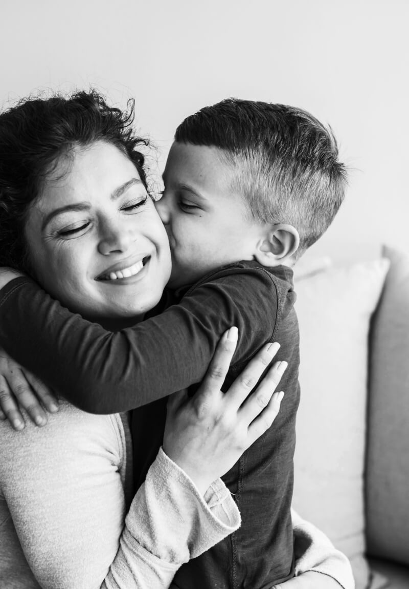 Mother smiling while holding her young son as he kisses her cheek