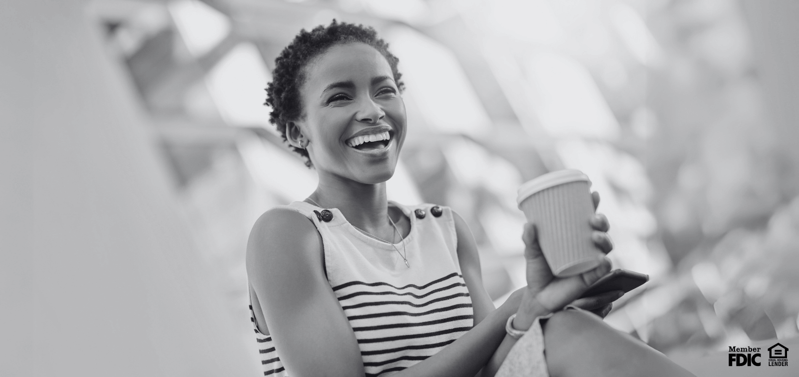 A young black woman sips coffee while viewing available homes on her phone.