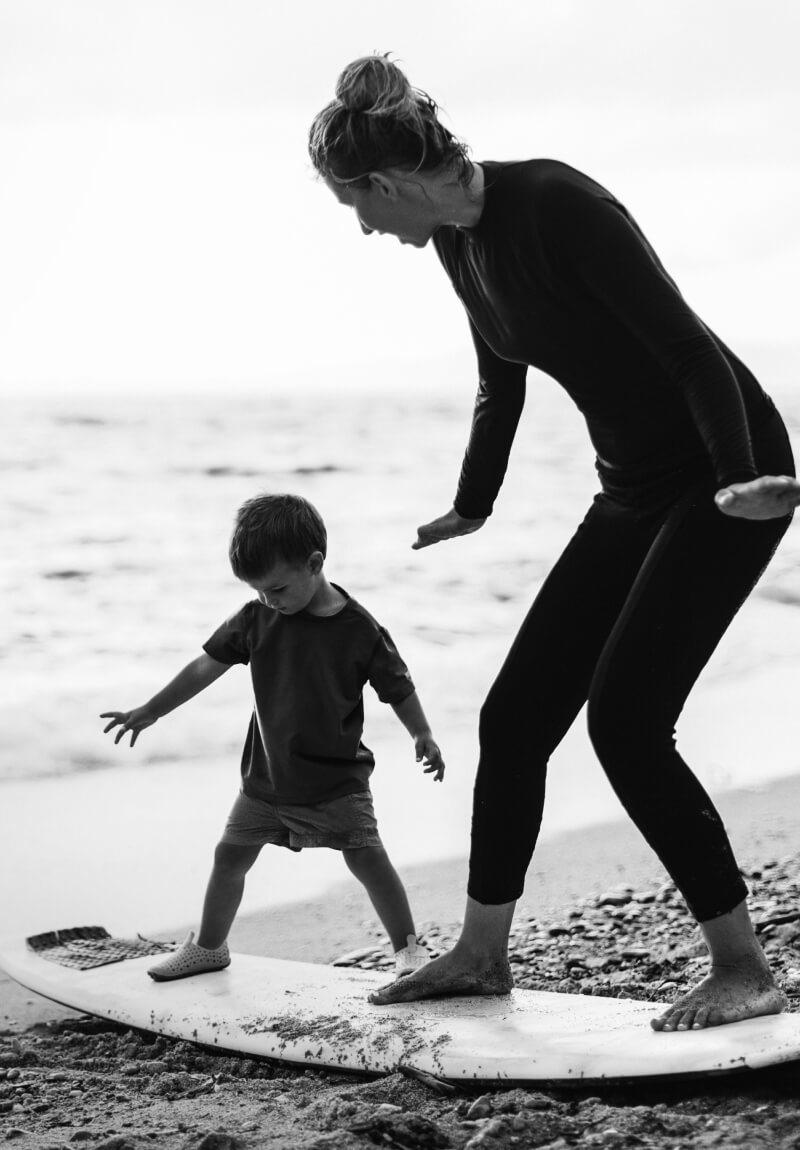 Mother and young son at the beach practicing standing on a surf board