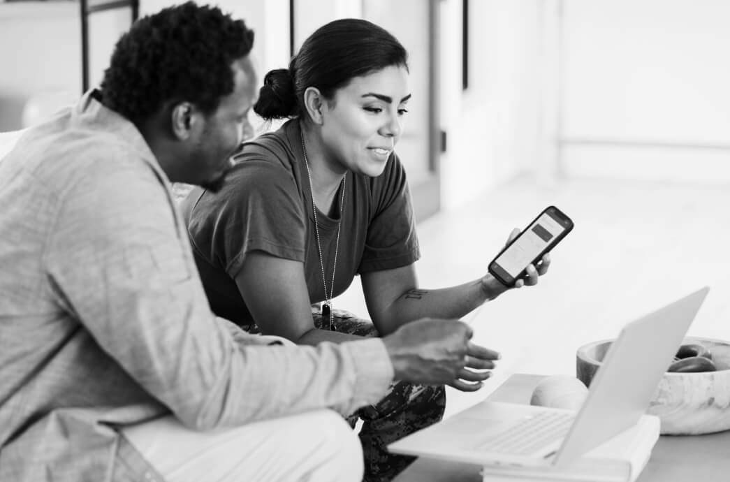 Couple sitting together while looking at laptop and smart phone