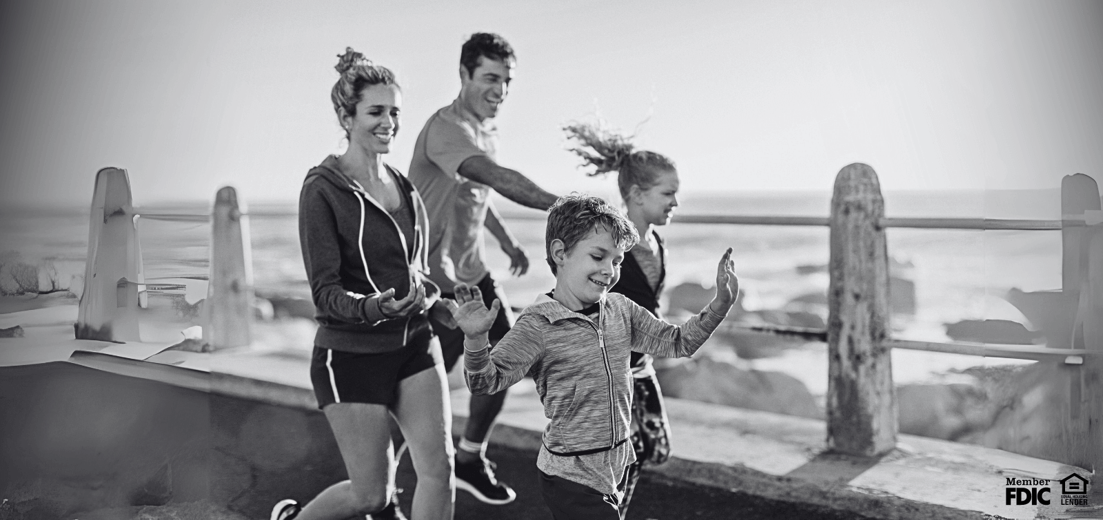 A family run down a pier next to the water.
