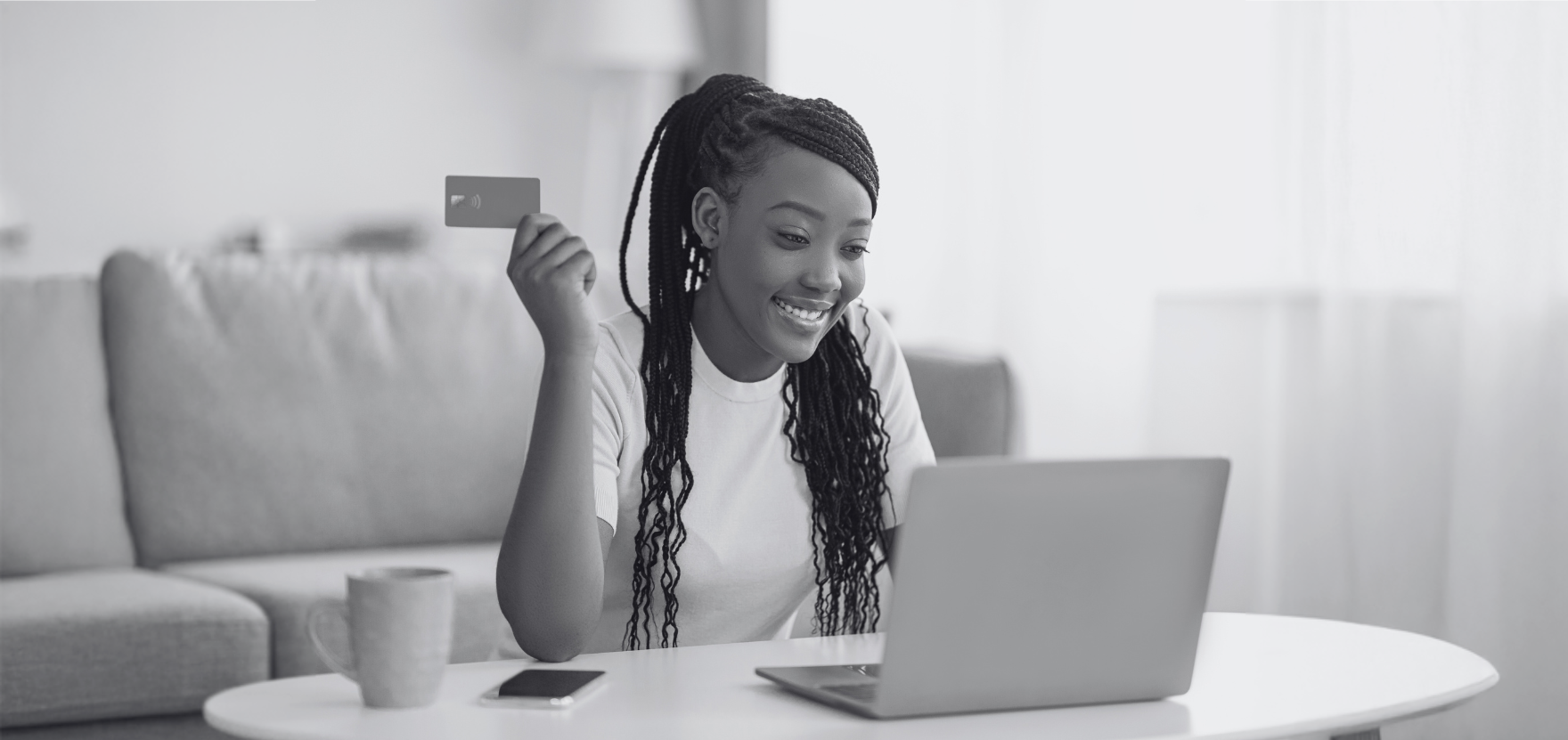 Young woman looking at her computer and holding a debit card while she looks at her free checking account online.