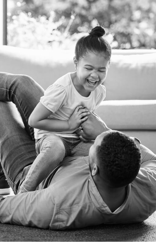 Father holding daughter on the floor of their living room while daughter is laughing